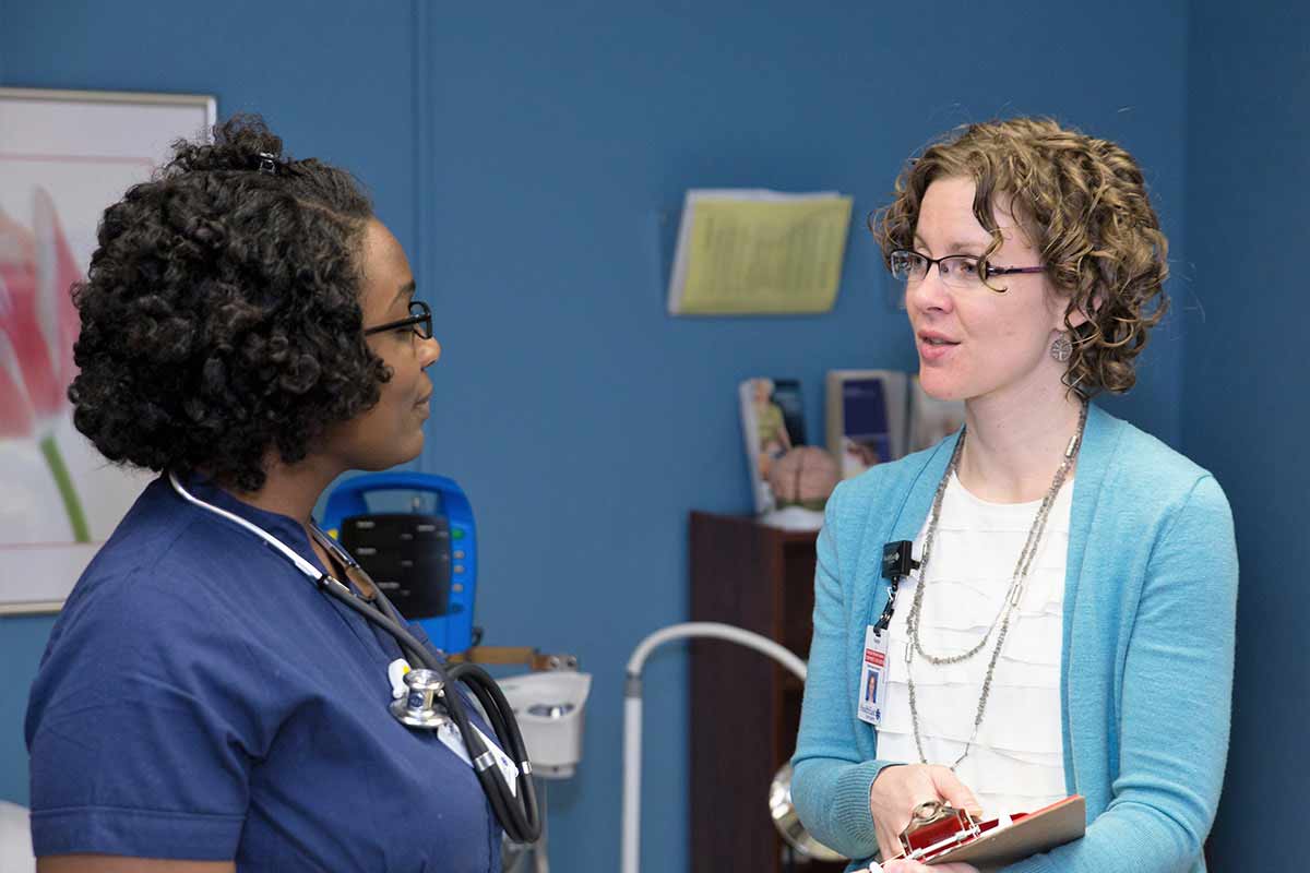 Two nurses talk to each other in a hospital setting.