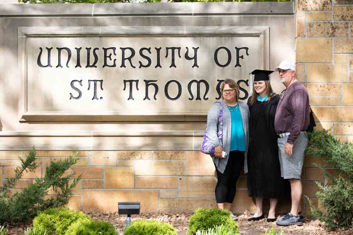 parents and their student stand by a concrete sign that says University of St Thomas