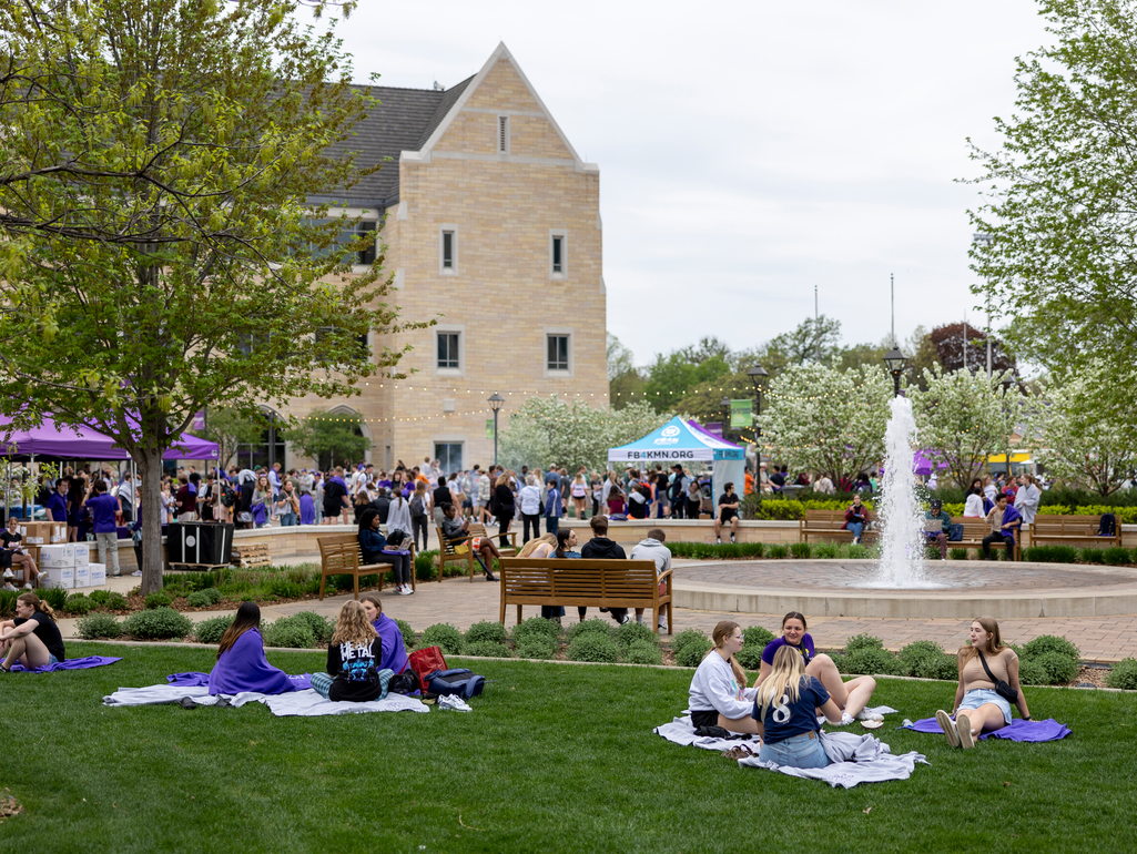 students sit on the grass near the fountain