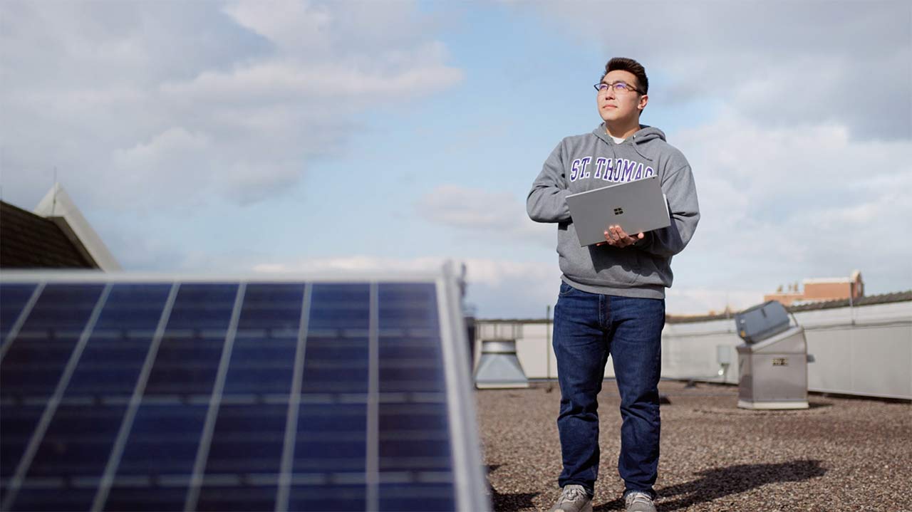 A student stands on the roof next to solar panels
